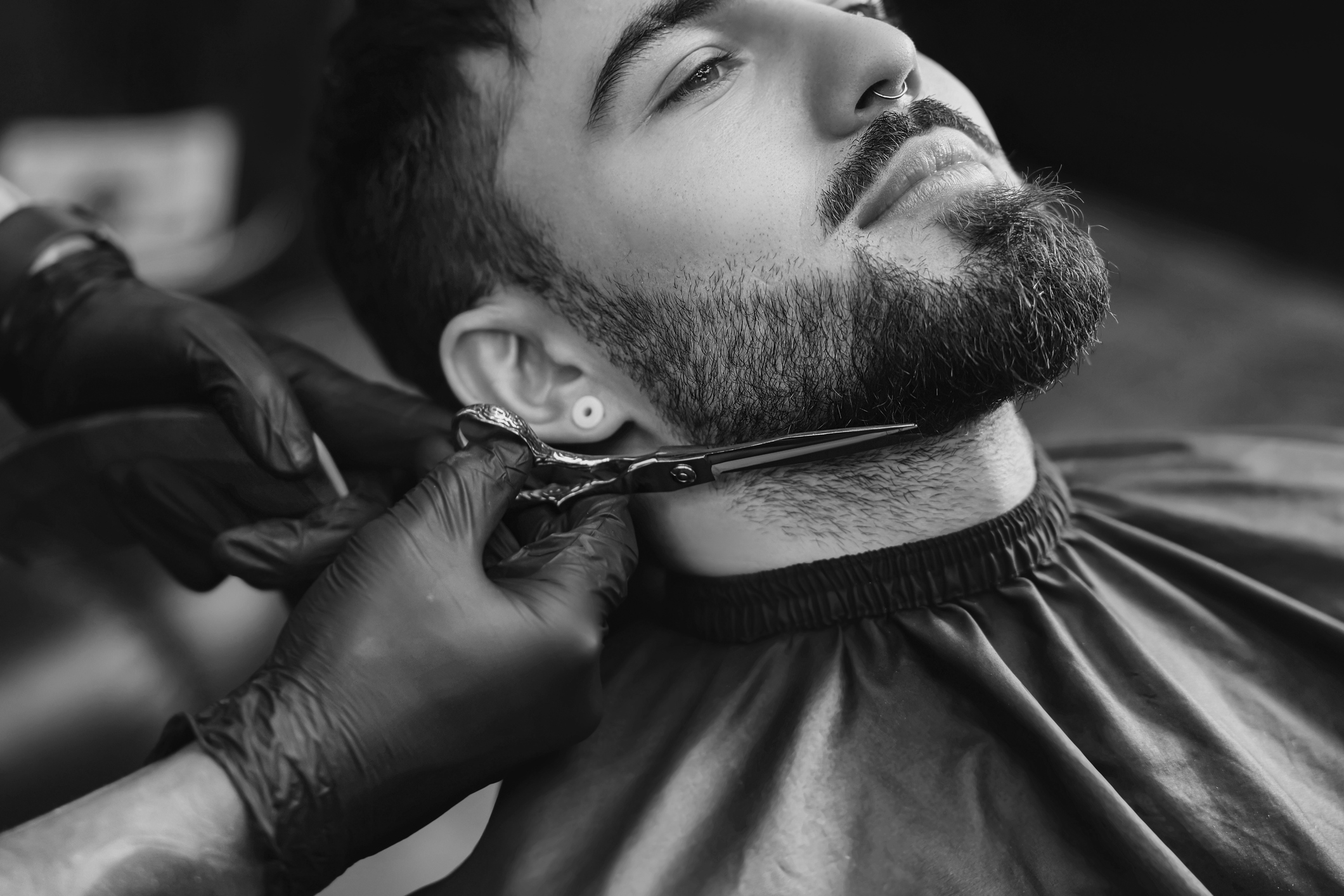 Professional hairdresser working with bearded client in barbershop, closeup. Black and white effect | Mr Who Barber Shop